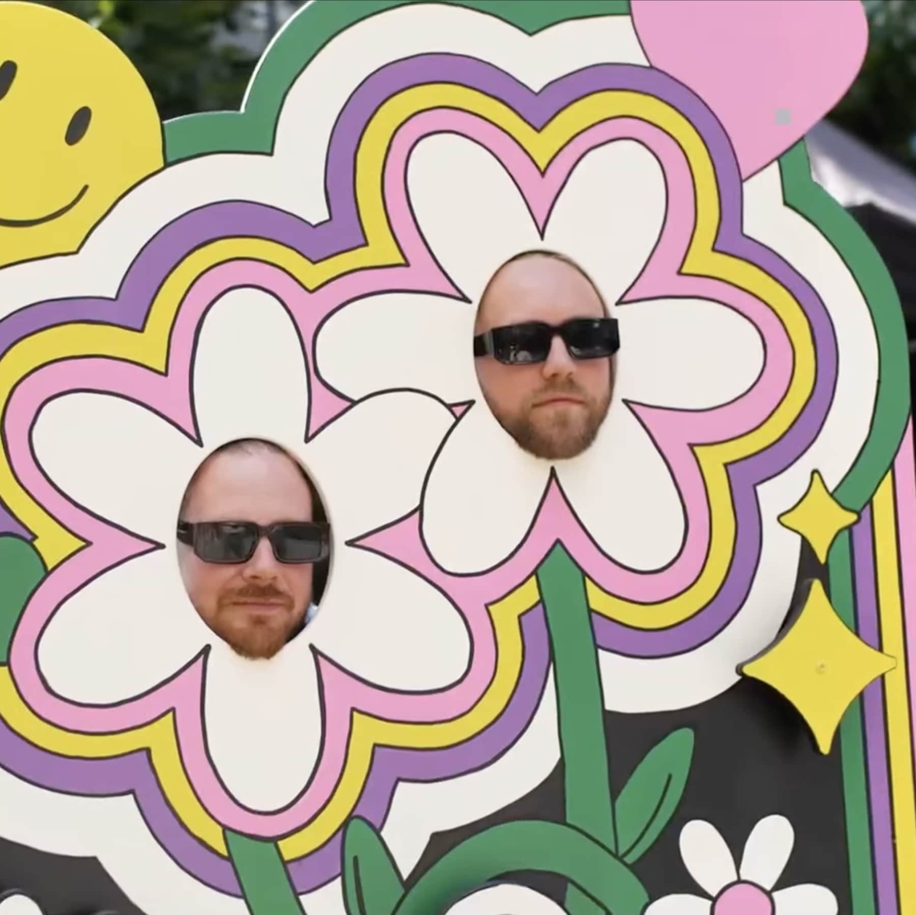 Cutout board with colourful flowers and two bearded men with sunglasses looking through